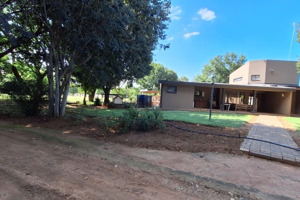Rear view of the property featuring a covered patio, paved walkway, and a spacious garden with mature trees.