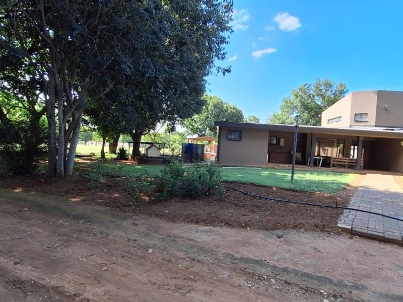 Rear view of the property featuring a covered patio, paved walkway, and a spacious garden with mature trees.