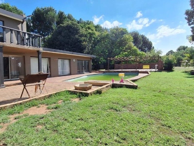 Rear exterior view featuring a swimming pool, brick paved patio area, and a balcony overlooking the garden with mature trees.