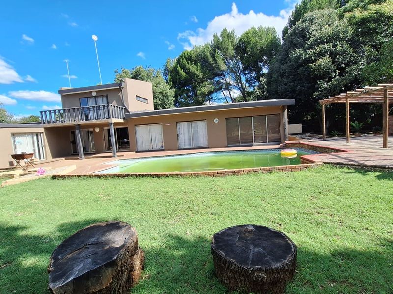 Rear view of the property featuring a swimming pool, a wooden pergola, and a balcony overlooking the garden and paved patio area.