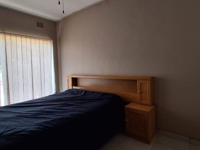 A bedroom featuring a built-in wooden headboard, vertical window blinds, and tiled flooring, requiring cosmetic updates to improve its overall appeal.