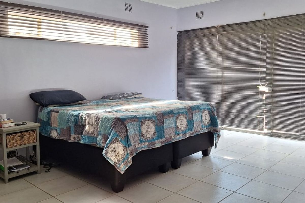 Spacious bedroom featuring tiled flooring, large sliding glass doors with venetian blinds, and ample natural light.