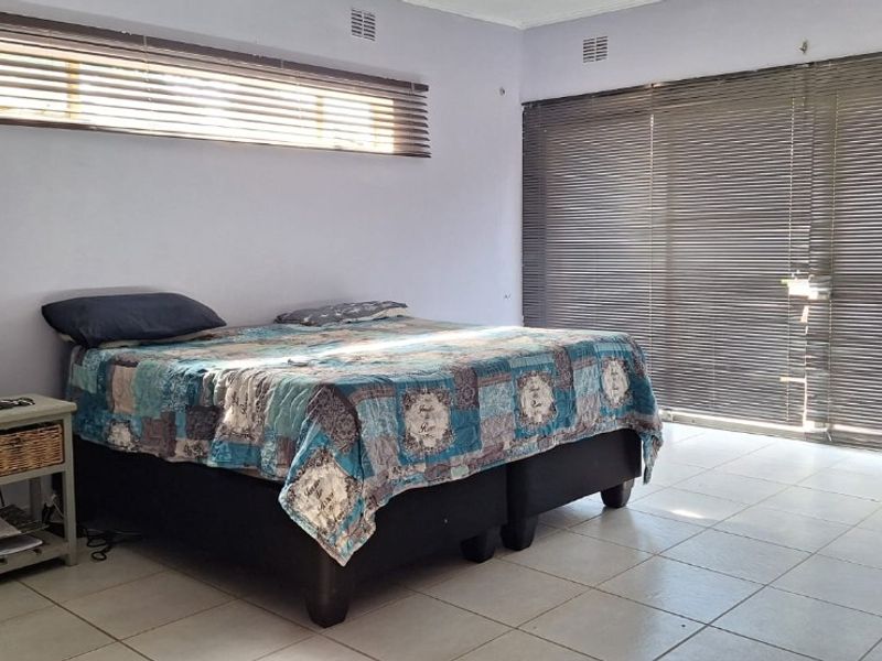 Spacious bedroom featuring tiled flooring, large sliding glass doors with venetian blinds, and ample natural light.