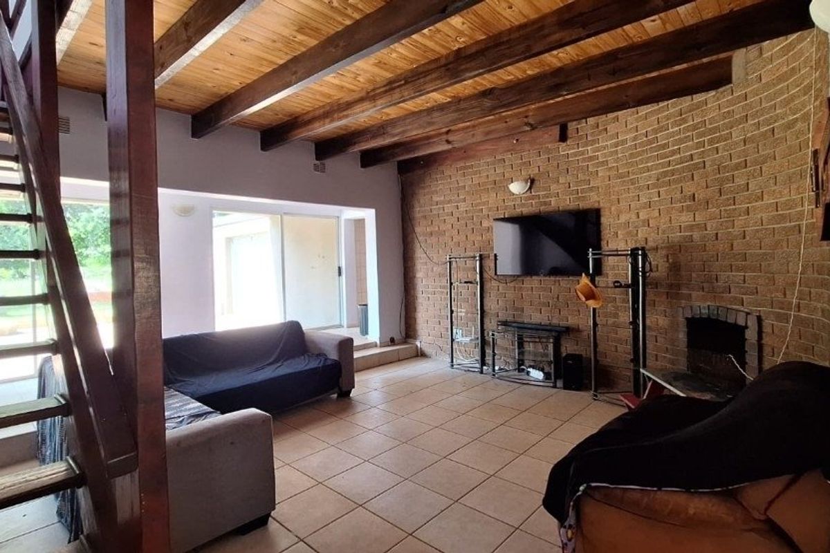 Spacious living room featuring exposed timber ceiling beams, a rustic brick feature wall with a built-in fireplace, tiled flooring, and access to the patio.