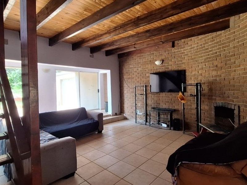 Spacious living room featuring exposed timber ceiling beams, a rustic brick feature wall with a built-in fireplace, tiled flooring, and access to the patio.