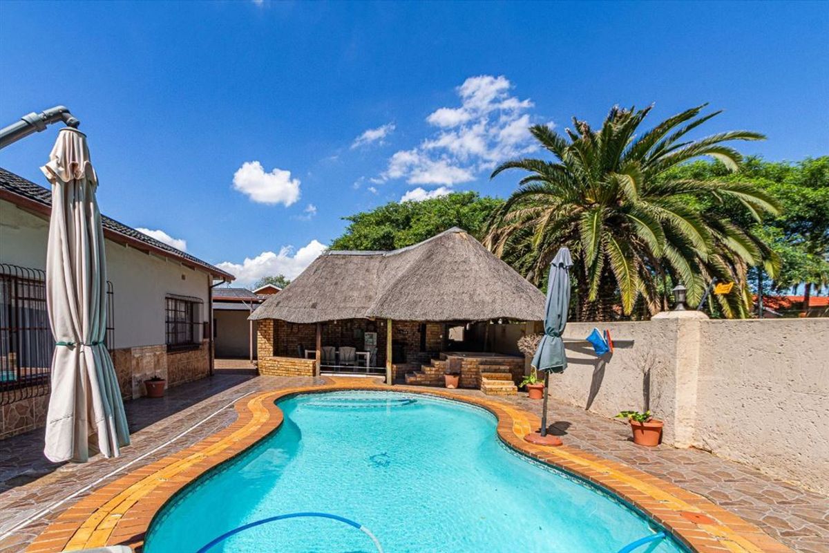Outdoor pool area featuring a swimming pool, paved surround, and a traditional thatched lapa for entertainment.