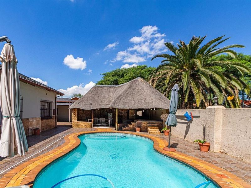 Outdoor pool area featuring a swimming pool, paved surround, and a traditional thatched lapa for entertainment.