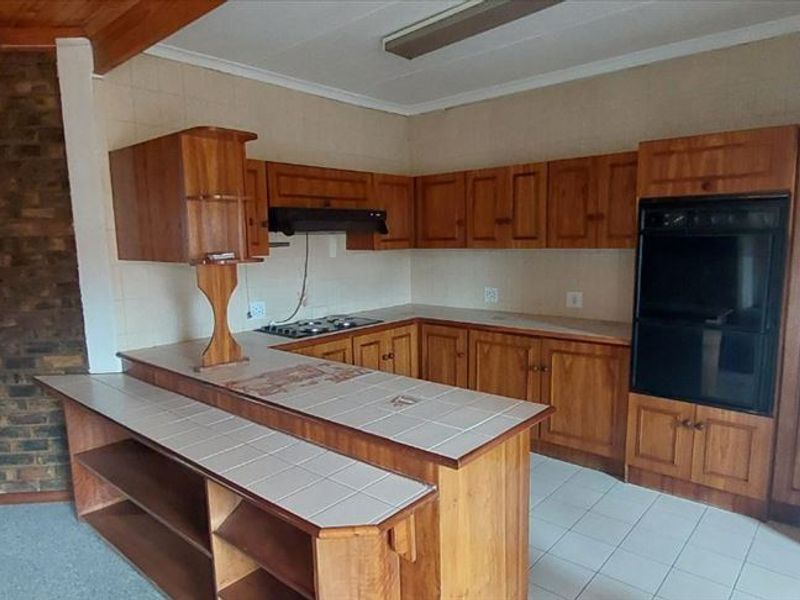 A dated kitchen featuring wooden cabinetry, tiled countertops, built-in oven, hob, and a distinctive brick feature wall, offering potential for modern renovation.