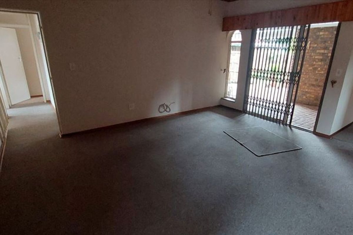 An empty living room featuring carpet flooring, a security gate leading to the exterior, and an arched doorway.
