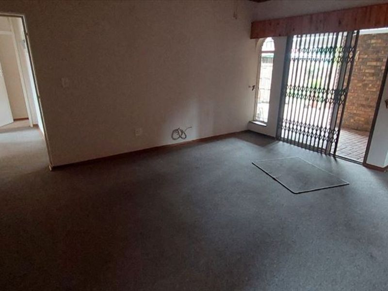 An empty living room featuring carpet flooring, a security gate leading to the exterior, and an arched doorway.