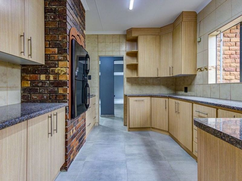 A functional kitchen featuring light wood cabinetry, granite countertops, a built-in double oven, and a distinctive exposed brick feature wall.