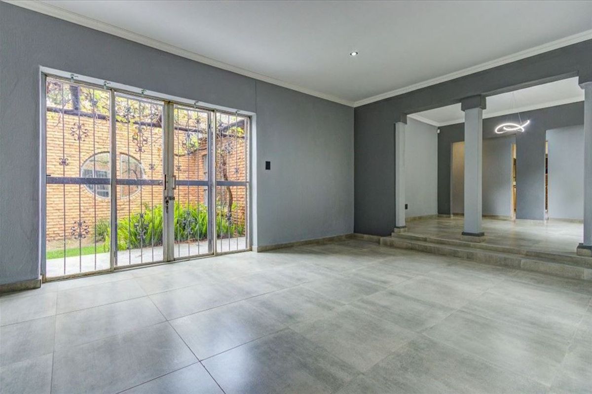 Spacious, empty living area featuring large format floor tiles, recessed lighting, and sliding glass doors opening to a private garden courtyard.
