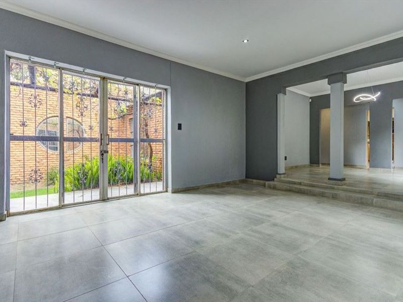 Spacious, empty living area featuring large format floor tiles, recessed lighting, and sliding glass doors opening to a private garden courtyard.