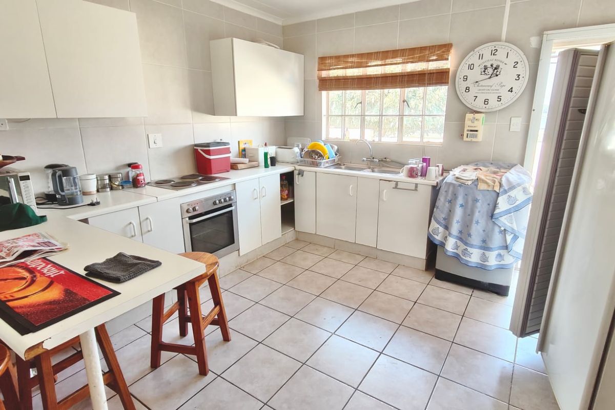 A functional kitchen featuring white cabinetry, tiled flooring, a built-in oven and hob, and a stainless steel sink with a window view.