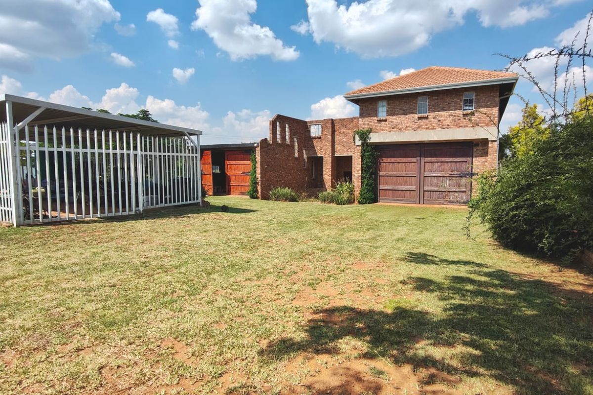 Rear view of the property featuring a brick facade, double garage, attached carport, and a spacious lawn area.