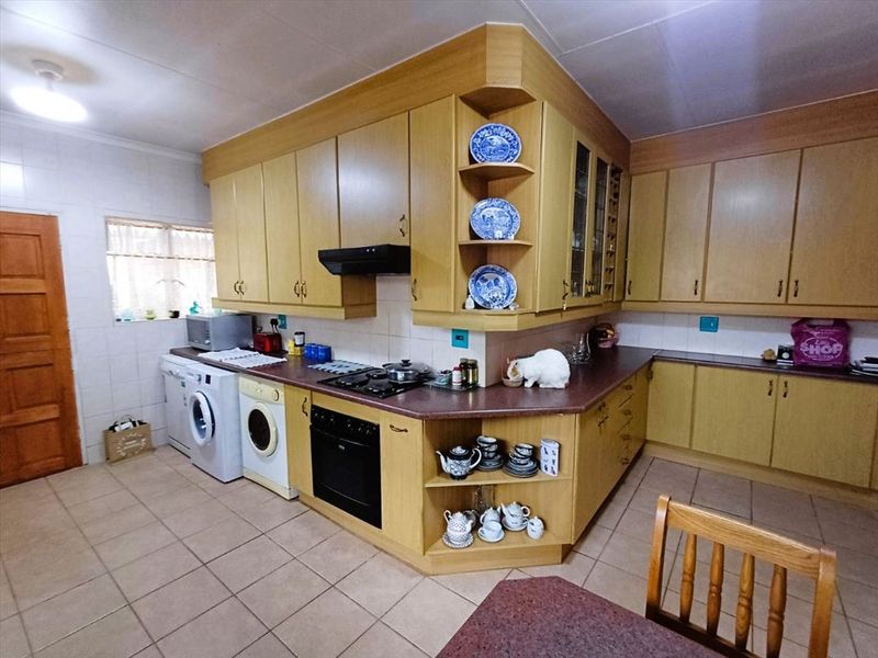 A functional kitchen featuring light wood-tone cabinetry, laminate countertops, built-in oven, gas hob, and tiled flooring with integrated laundry appliance space.