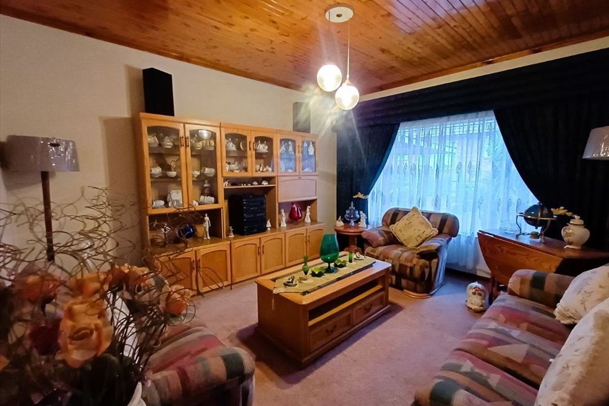 A cozy living room featuring a warm timber tongue and groove ceiling, carpeted flooring, and a large window with curtains.
