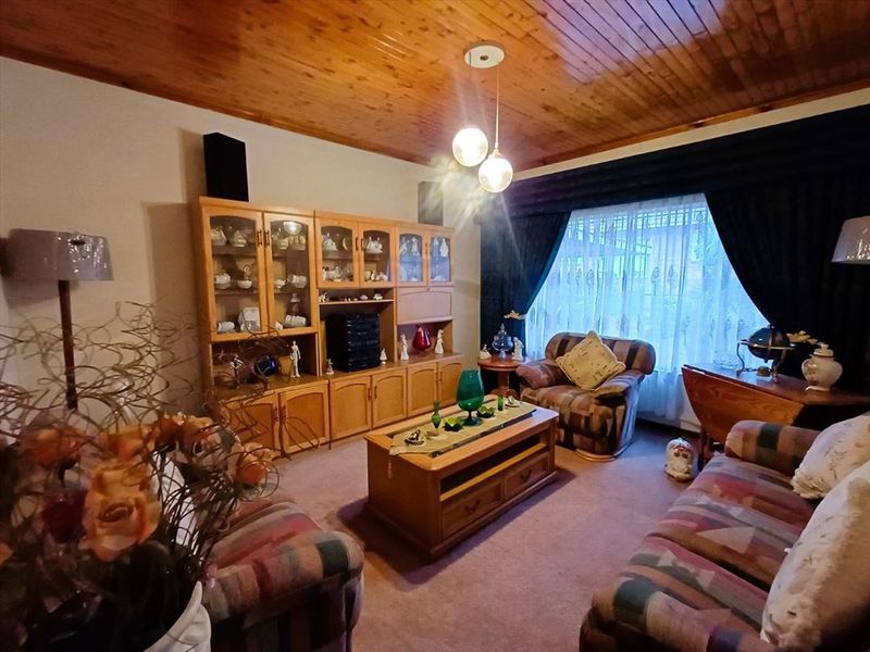 A cozy living room featuring a warm timber tongue and groove ceiling, carpeted flooring, and a large window with curtains.