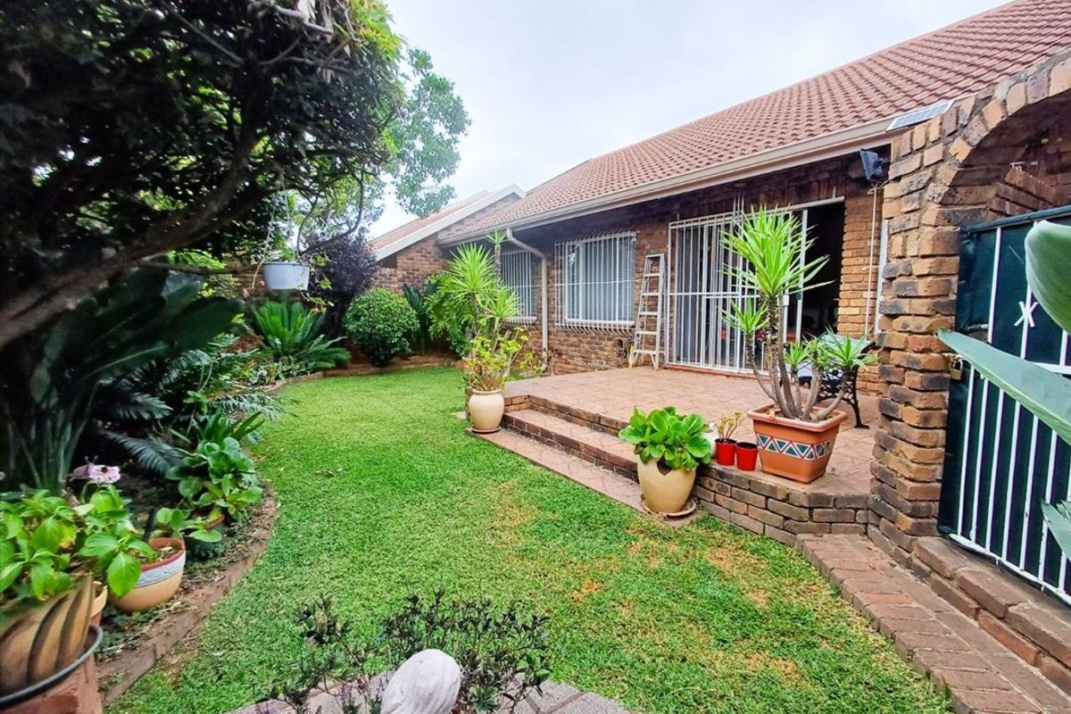 A rear view of the townhouse featuring a tiled patio area, brick exterior walls, security bars on windows, and a well-maintained garden.