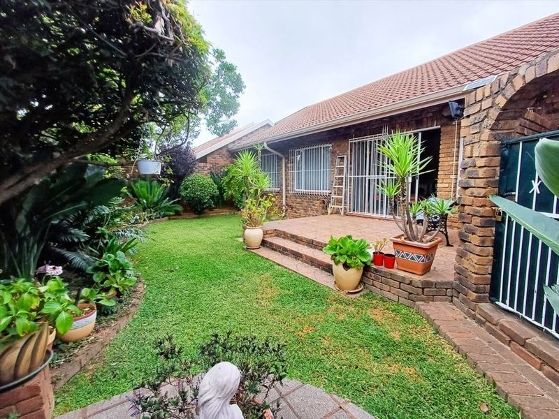 A rear view of the townhouse featuring a tiled patio area, brick exterior walls, security bars on windows, and a well-maintained garden.