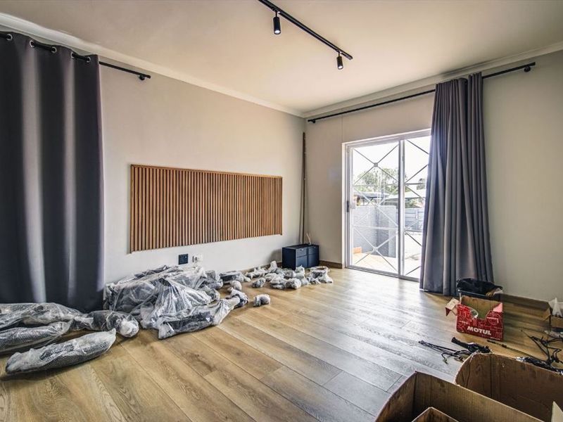 A bright living area featuring modern laminate flooring, track lighting, a decorative slatted wood wall panel, and direct access to the outdoors via sliding doors.