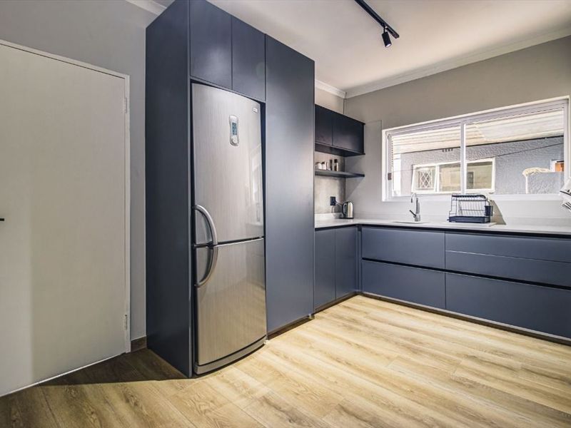 Modern kitchen featuring dark blue cabinetry, stone countertops, stainless steel sink, and light wood-look laminate flooring with efficient track lighting.
