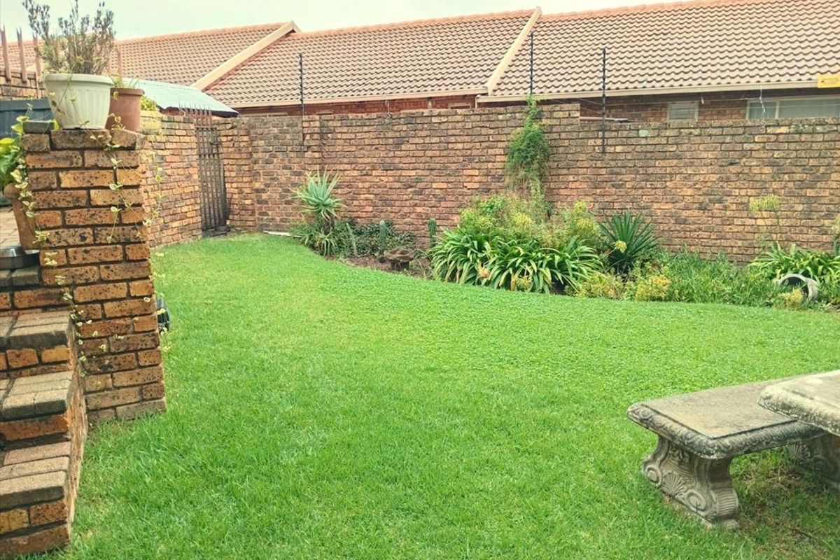 A private rear garden featuring a well-maintained lawn, established garden beds, and a secure brick boundary wall.