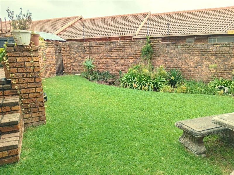 A private rear garden featuring a well-maintained lawn, established garden beds, and a secure brick boundary wall.