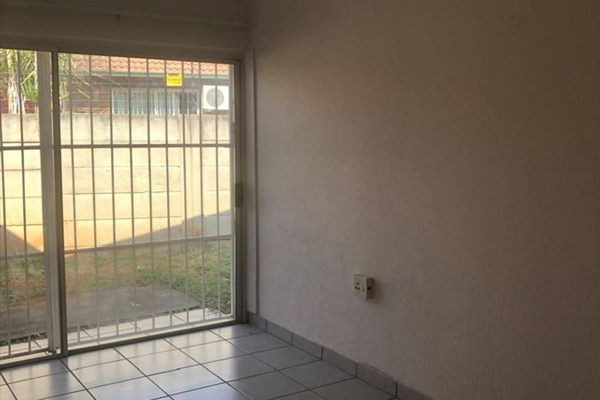 An empty living room featuring tiled flooring and a sliding glass door with security bars, providing direct access to the outdoor area.