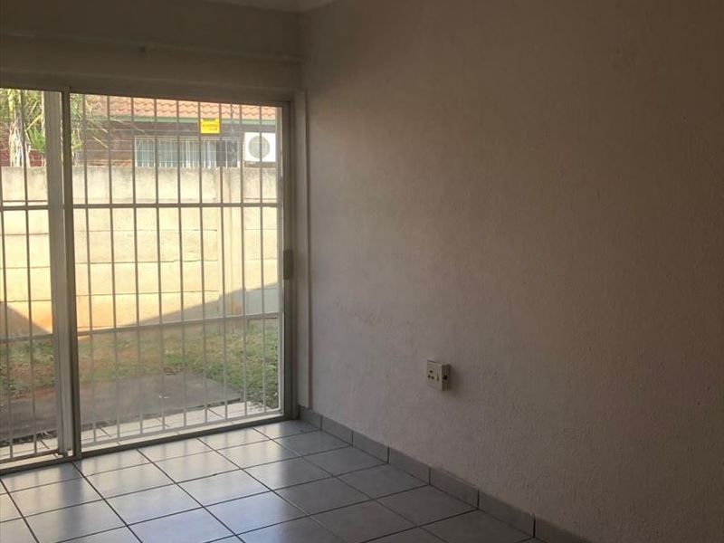 An empty living room featuring tiled flooring and a sliding glass door with security bars, providing direct access to the outdoor area.