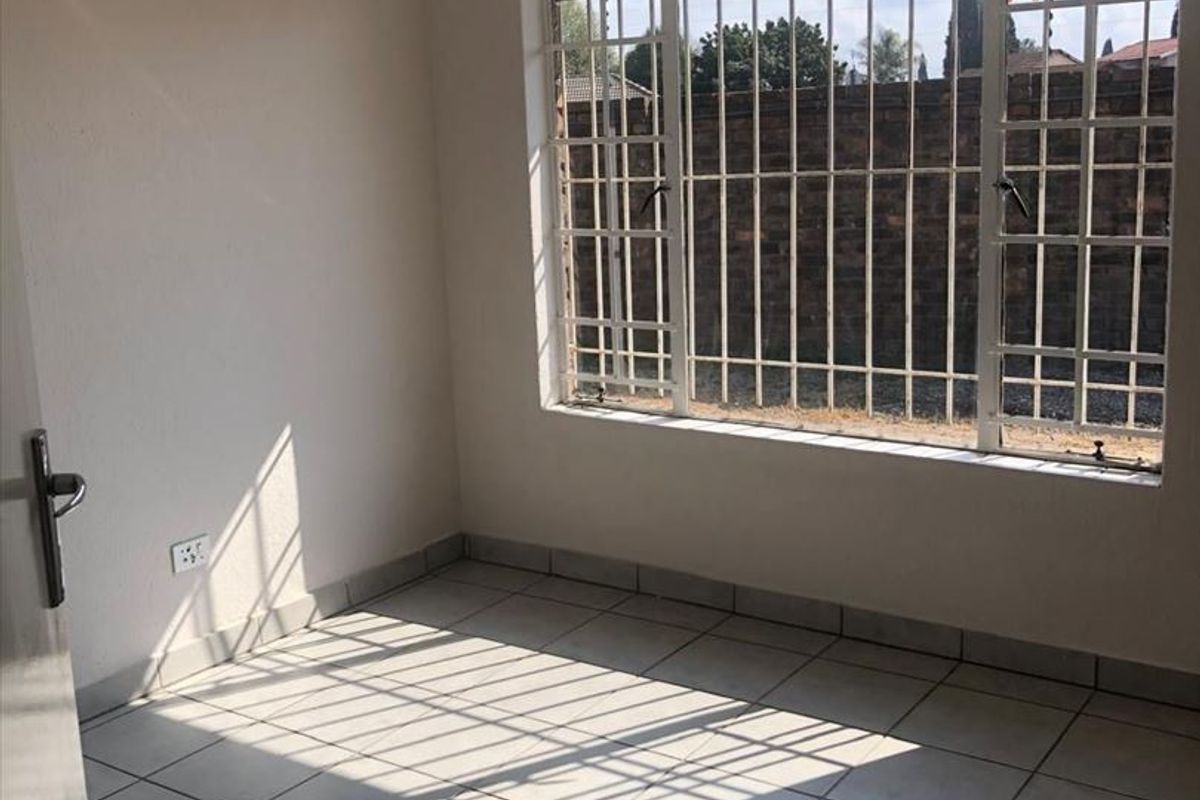 A bright, empty bedroom featuring neutral tiled flooring, recessed downlights, and large windows fitted with security bars.
