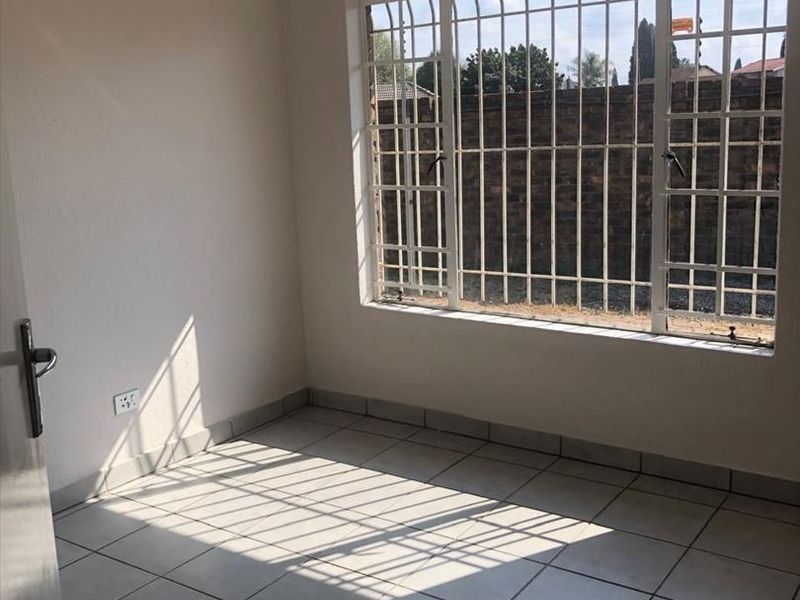 A bright, empty bedroom featuring neutral tiled flooring, recessed downlights, and large windows fitted with security bars.