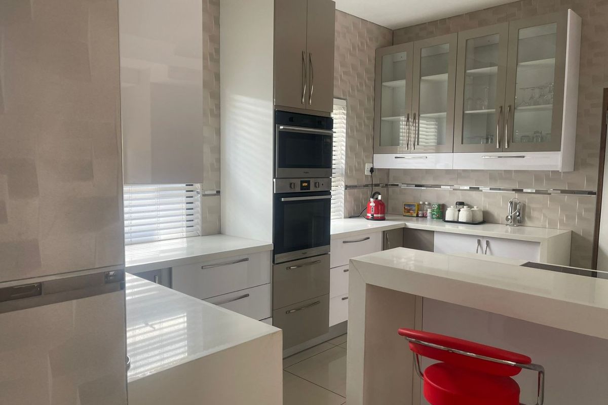 Modern kitchen featuring high-gloss cabinetry, integrated oven and microwave, quartz countertops, and a functional breakfast bar with a tiled backsplash.