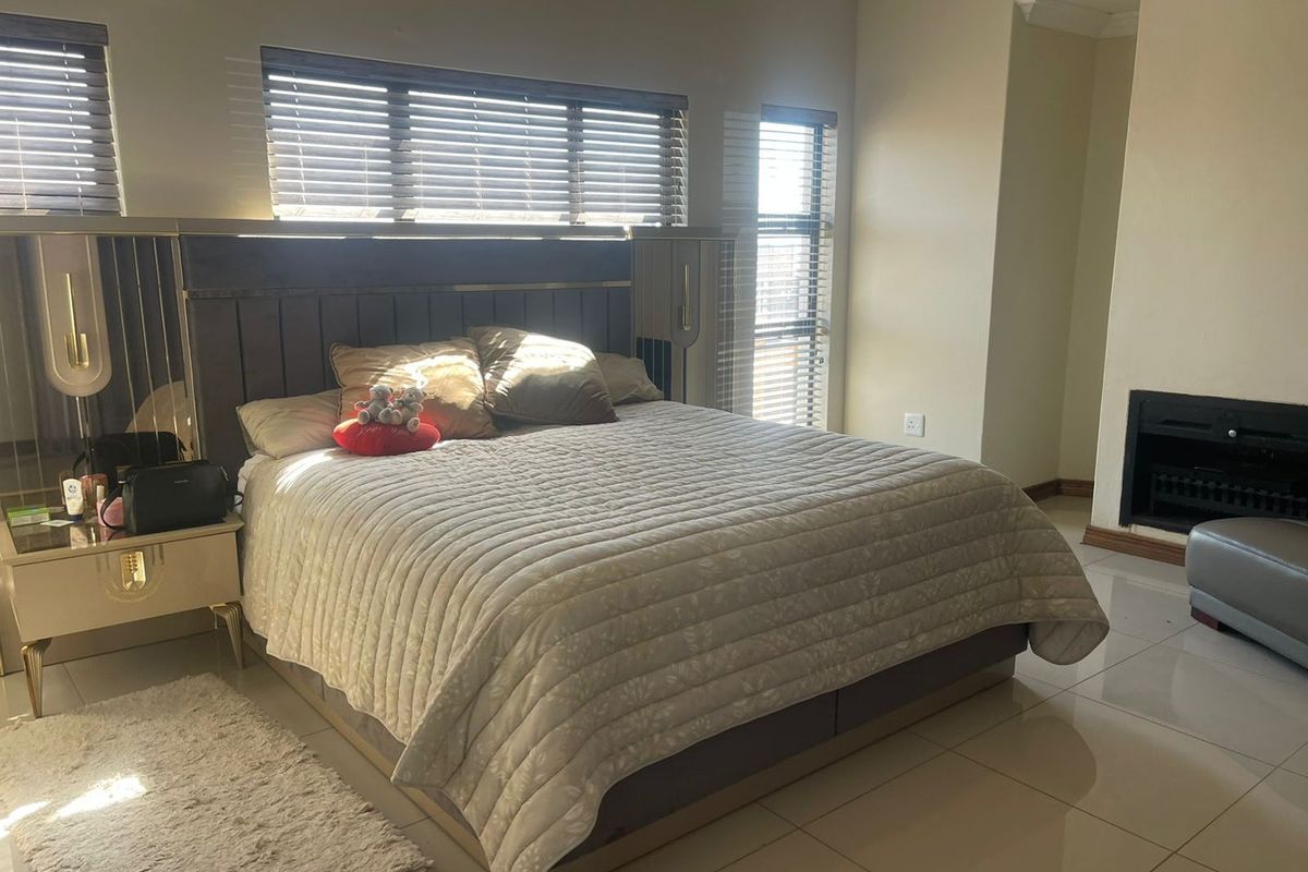 Spacious bedroom featuring tiled flooring, a built-in fireplace, and large windows with venetian blinds, offering a comfortable and well-lit living space.