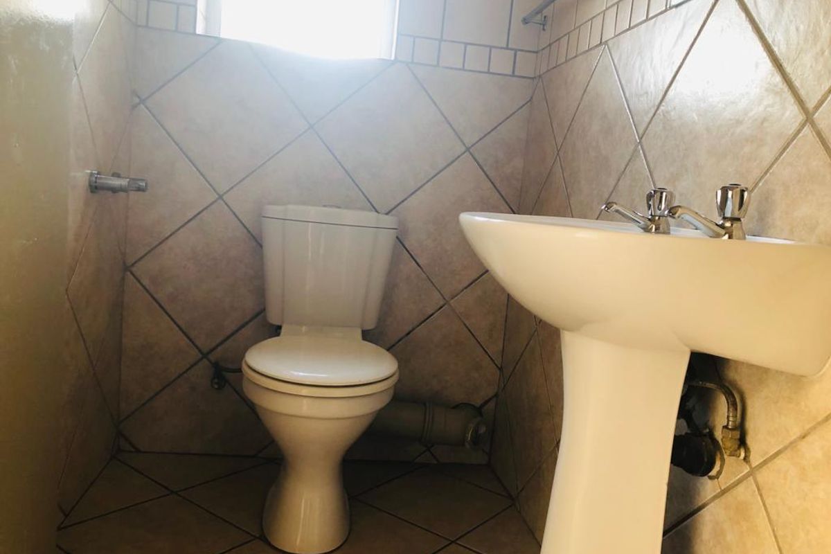 A compact bathroom featuring a pedestal basin and toilet with neutral tiled walls and flooring.