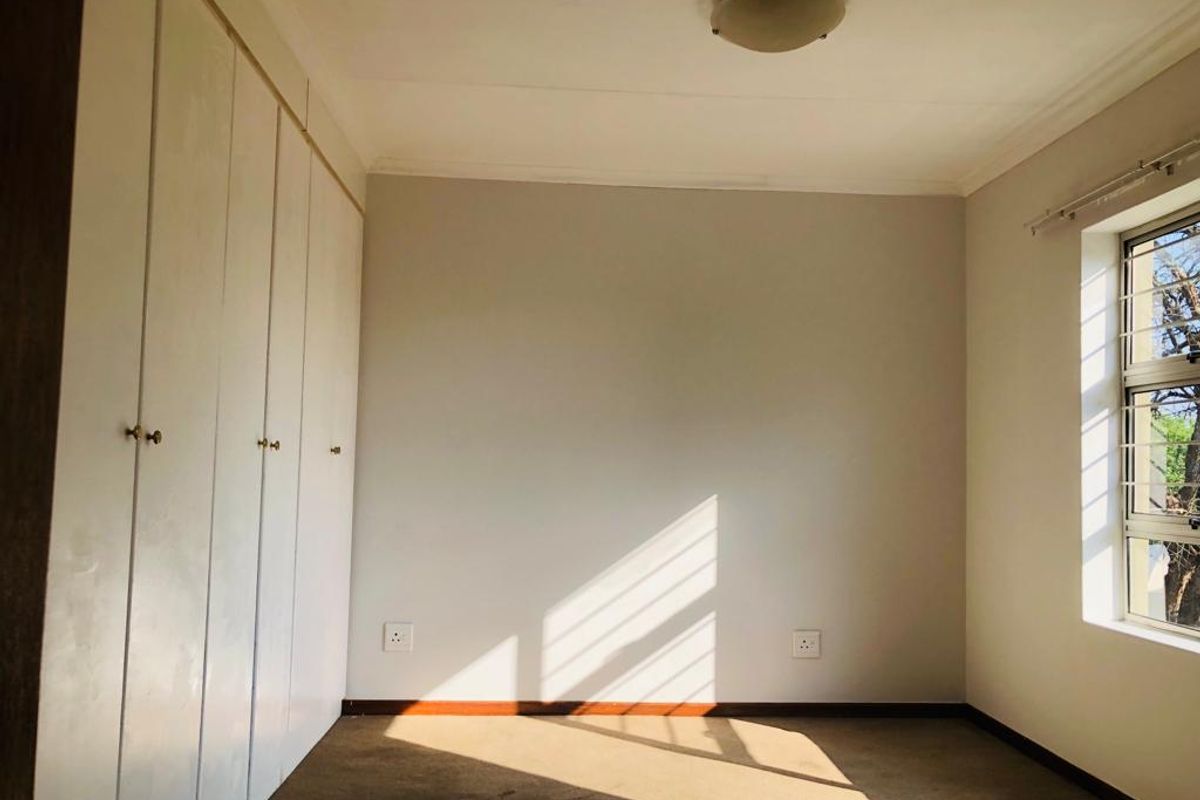 A bright, empty bedroom featuring built-in cupboards, carpeted flooring, and a window with security bars, offering a clean canvas for personalization.