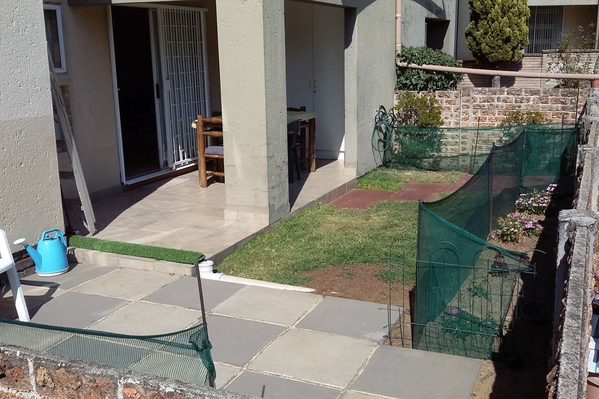Rear exterior view featuring a covered patio, paved terrace area, and a private garden space enclosed by a brick boundary wall.