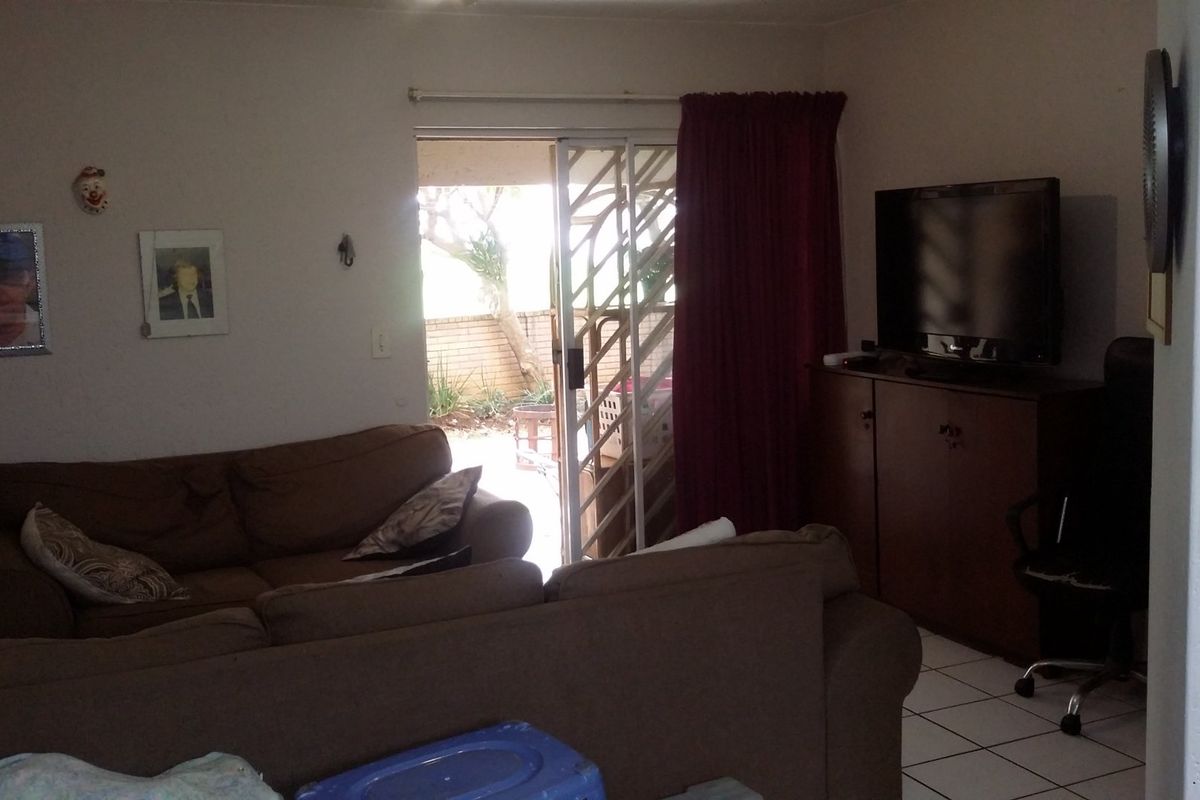 A living room area featuring tiled flooring and a sliding glass door with a security gate leading to an outdoor space.