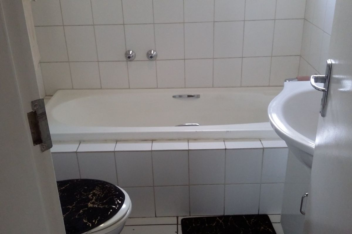 A compact bathroom featuring a built-in bathtub, pedestal washbasin, and tiled finishes, offering a functional space in need of cosmetic updates.