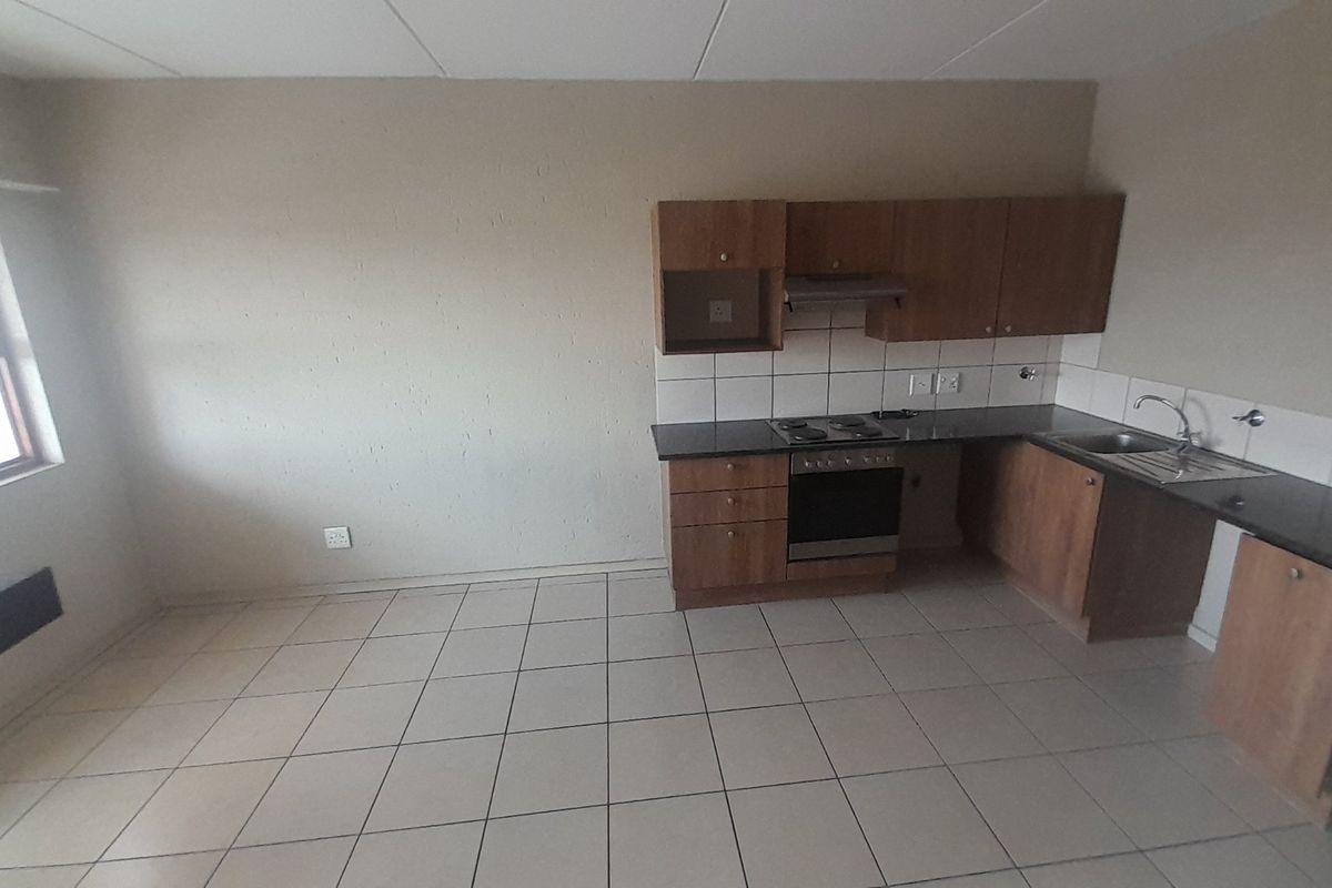 An empty kitchen featuring built-in wooden cabinetry, dark countertops, a built-in oven with hob, and tiled flooring throughout.