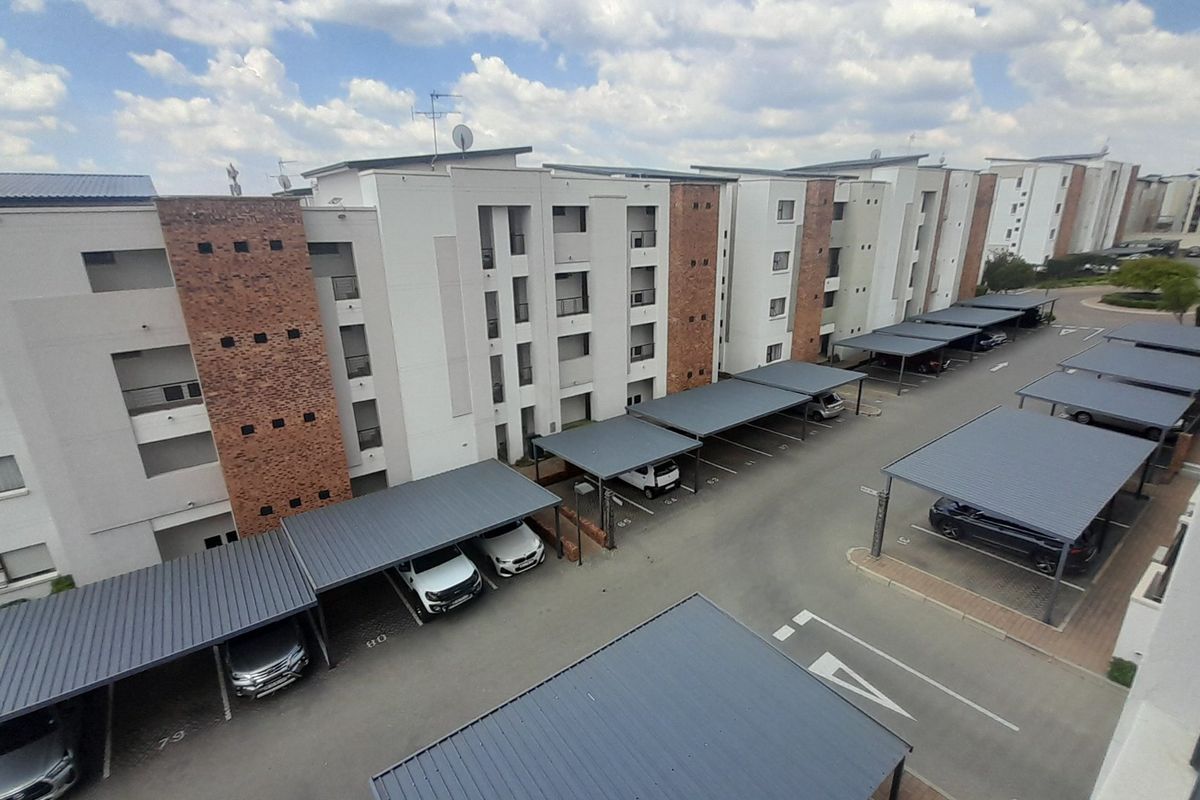 An elevated aerial view of a modern apartment complex featuring multiple covered parking bays and well-maintained building facades.