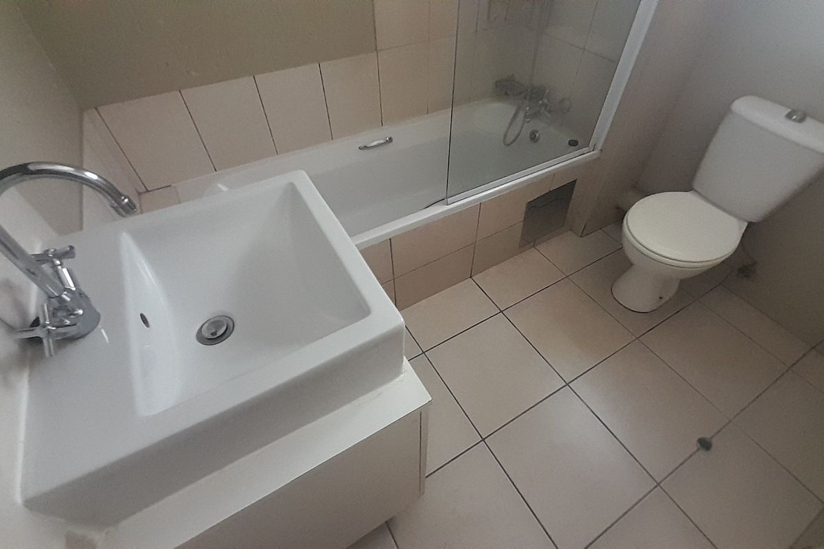 A functional bathroom featuring a vanity basin, bathtub with glass screen, and toilet, finished with neutral ceramic tiling.