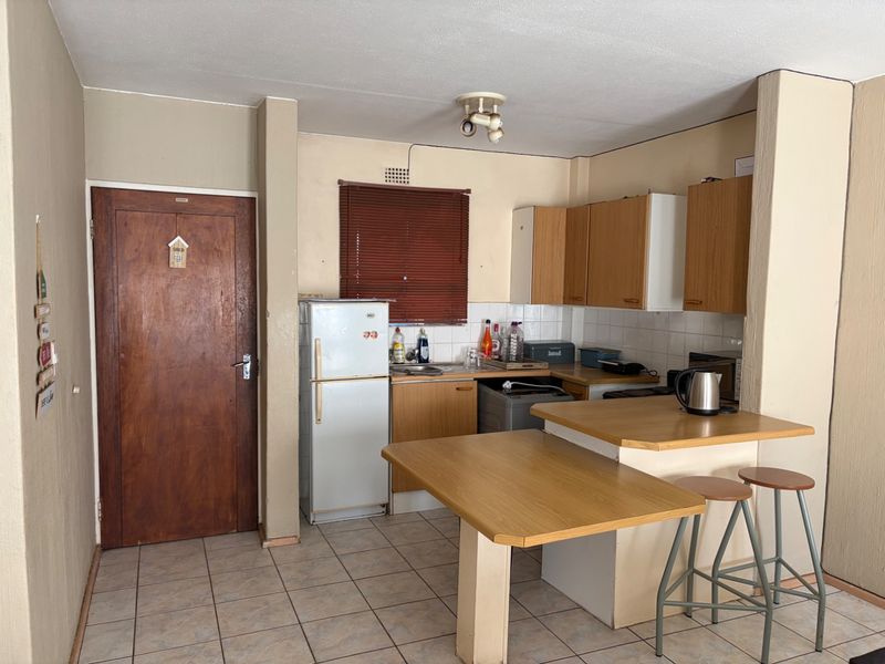 A compact kitchen featuring laminate cabinetry, a breakfast bar, tiled flooring, and a tiled backsplash, offering a functional layout in need of cosmetic updates.
