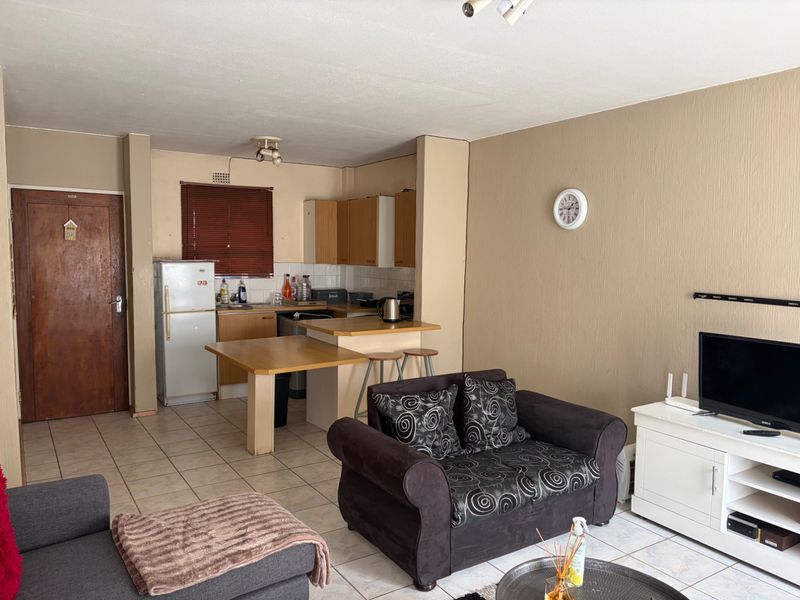 Open-plan living area featuring a combined kitchen with breakfast bar and tiled flooring throughout, offering a functional layout for modern apartment living.
