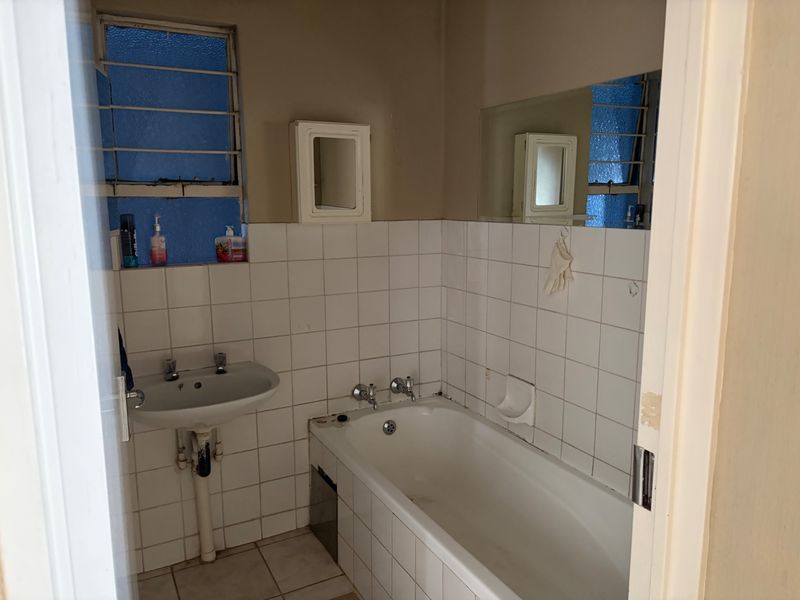 A dated bathroom featuring a standard bathtub, pedestal basin, and tiled finishes, requiring cosmetic updates to modernize the space.