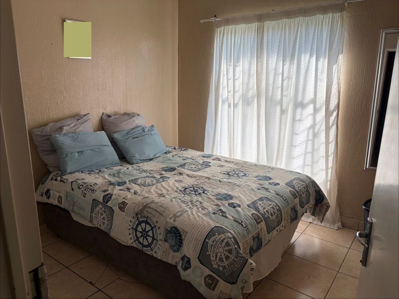 A compact bedroom featuring tiled flooring and a window with a curtain rail, offering a functional space ready for cosmetic updates.