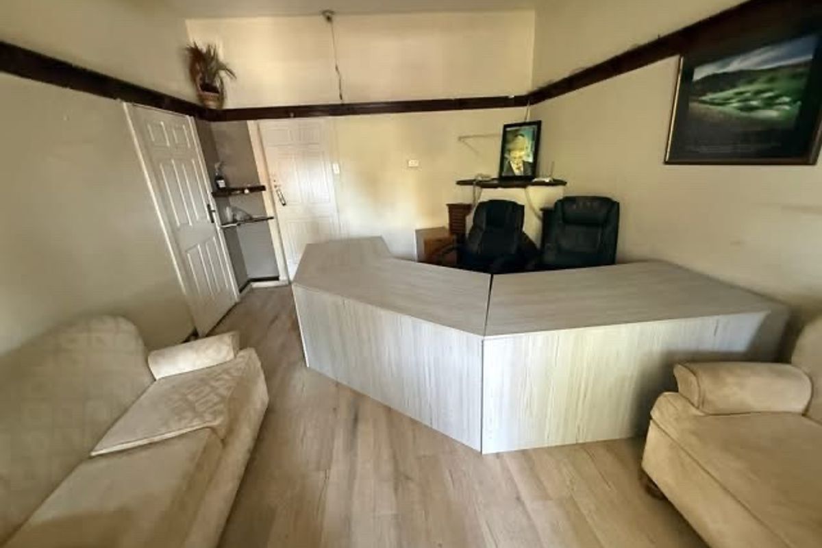 A functional living area featuring light wood-look flooring and a central built-in desk or counter unit, suitable for a home office or workspace.