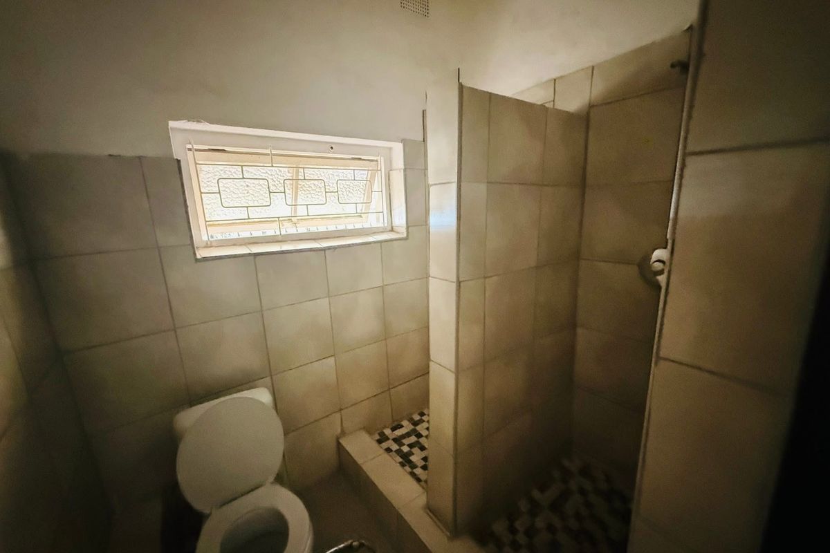 A functional bathroom featuring a tiled shower enclosure, a standard toilet, and a small window for ventilation.