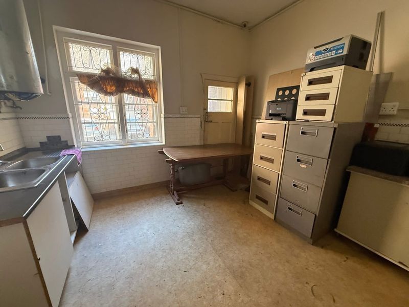A dated kitchen area featuring a double sink, tiled splashbacks, and a window with security bars, currently used as a utility or storage space.