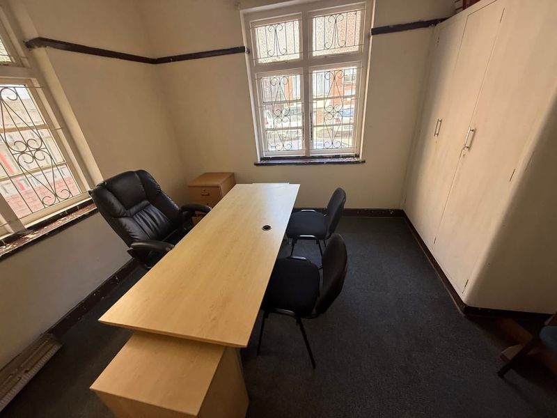 A functional office space featuring built-in storage cabinetry, dual windows with security bars, and carpeted flooring, suitable for a home workspace.